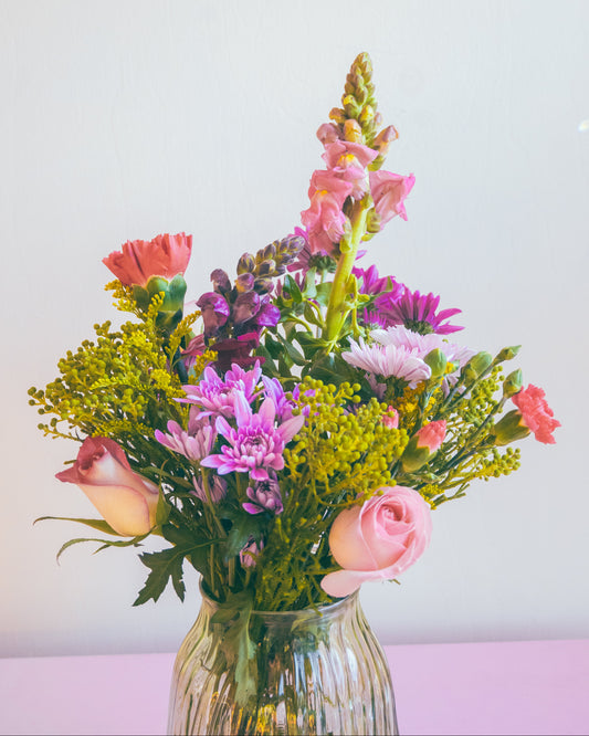 Bouquet of flowers in a clear vase on a light pink surface with a white background